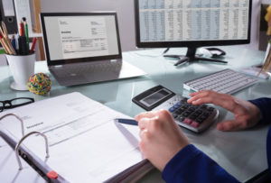 Man bookkeeping at a desk with a calculator book and computer