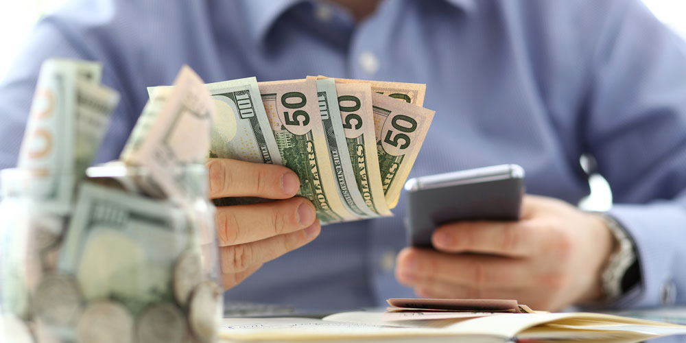 Male hand holding pack of banknotes and cellphone